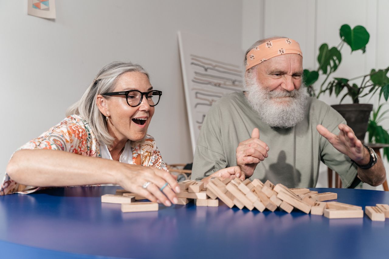 The Art of Drawing Readers In: Your attractive post title goes here Elderly couple laughing and bonding while playing Jenga indoors.