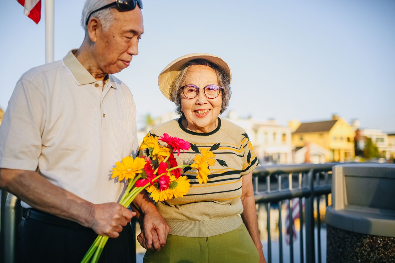 services-03 Happy elderly couple holding flowers outdoors, enjoying togetherness and love.