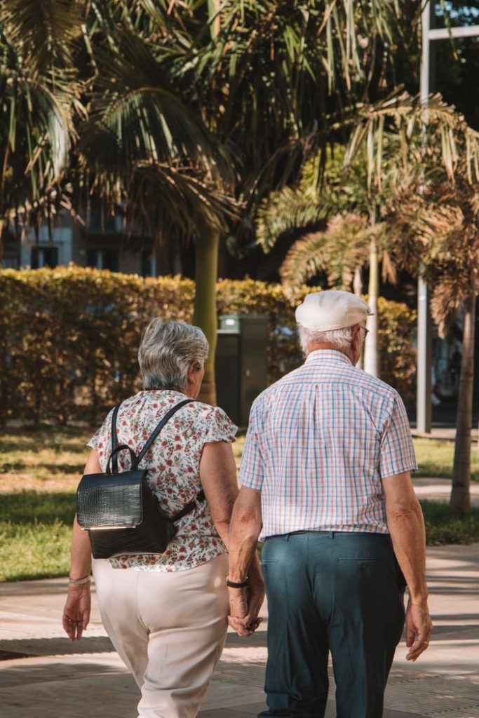Senior couple holding hands while walking in a sunny park in Málaga, Spain.