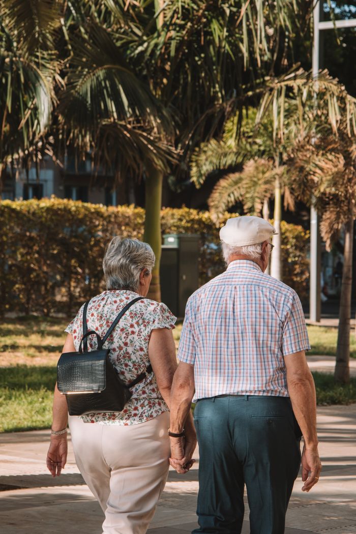 Senior couple holding hands while walking in a sunny park in Málaga, Spain.
