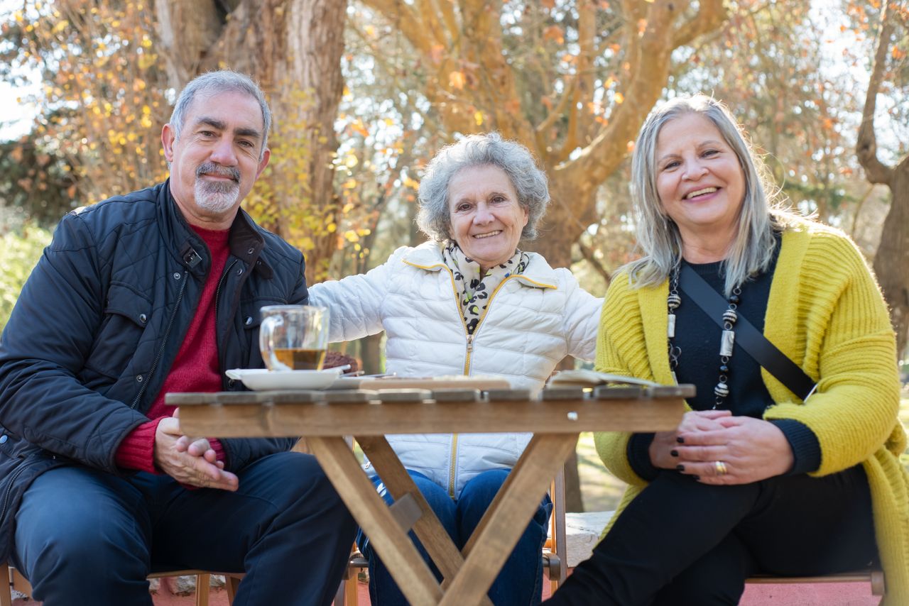 Three seniors enjoying a sunny outdoor gathering in Portugal, radiating happiness and companionship.