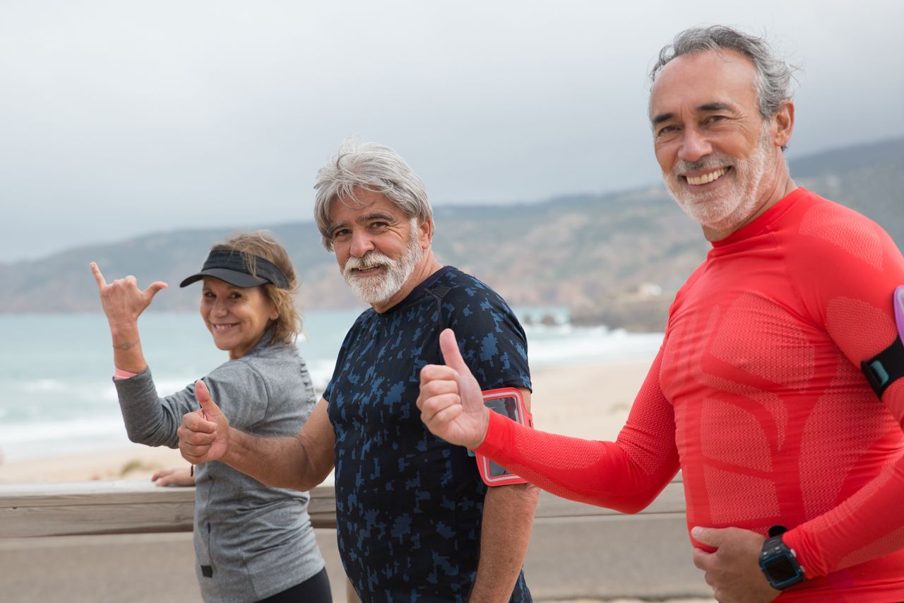 our-experience Smiling senior friends exercising on a beach in Portugal, embracing a healthy lifestyle.